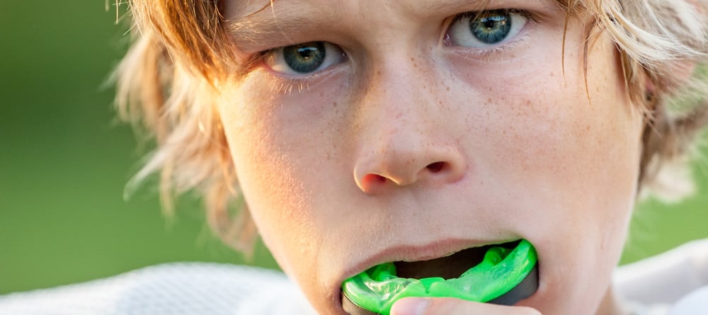 Close-up of a young boy in a sports jersey putting in his mouthguard