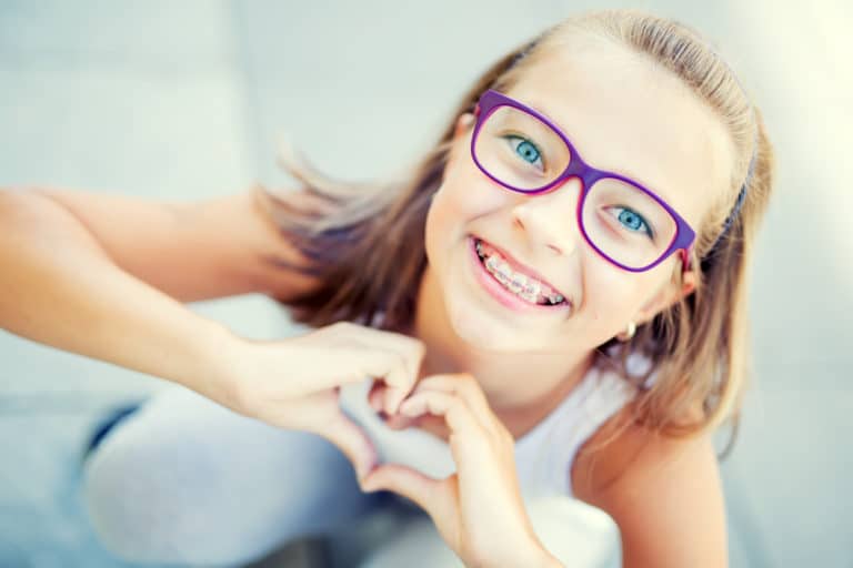 Smiling little girl with braces and glasses showing heart with hands